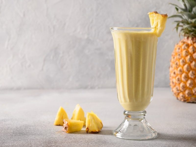 Ein Glas Ananas-Lassi vor einer frischen Ananas.