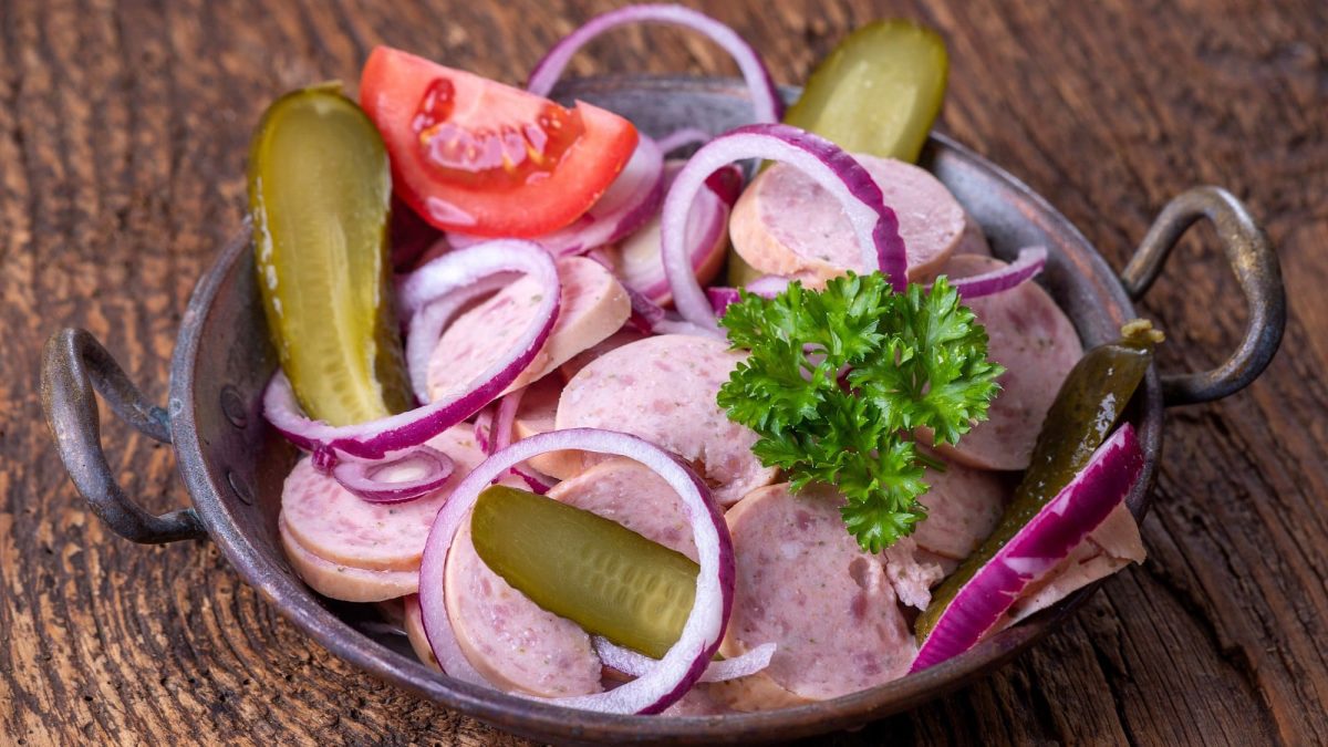 Draufsicht: eine Schüssel bayerischer Wurstsalat steht auf einem Tisch aus Holz.