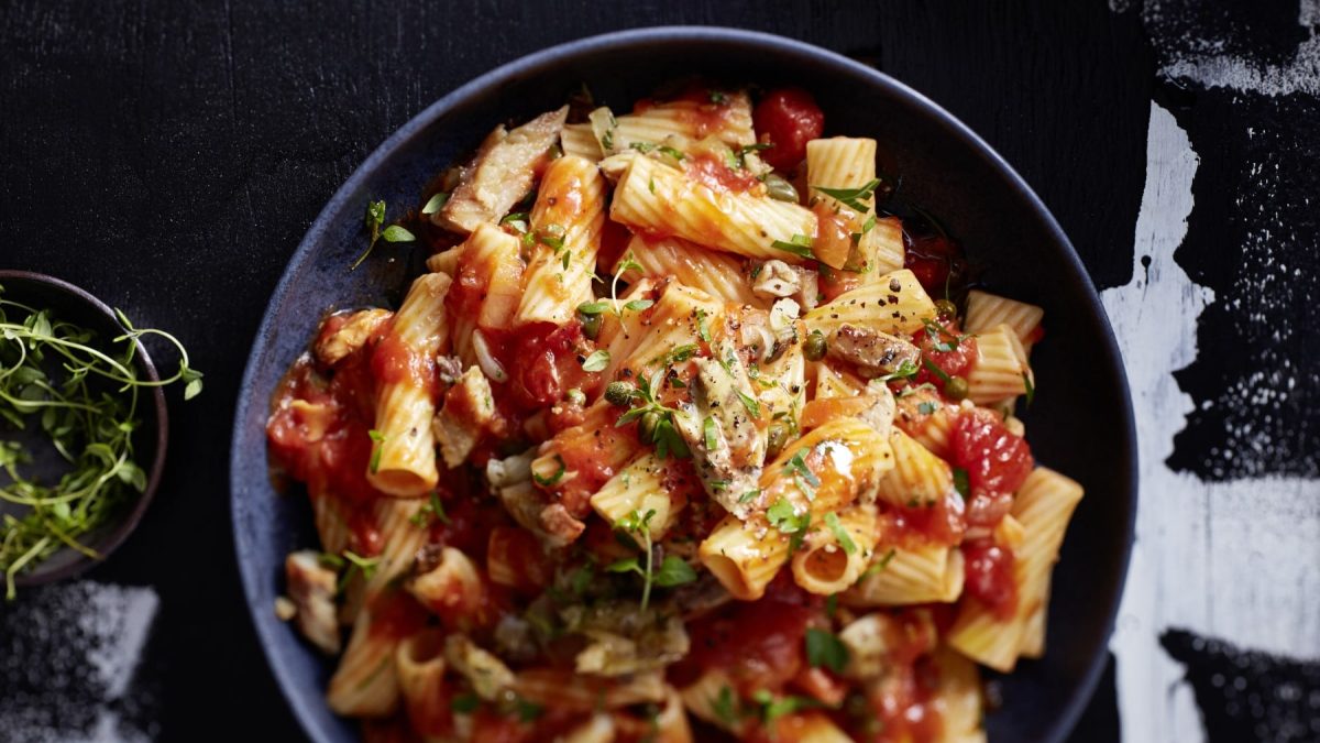 Eine dunkelblaue Bowl mit Pasta von oben fotografiert vor einem schwarz/weißen Hintergrund.