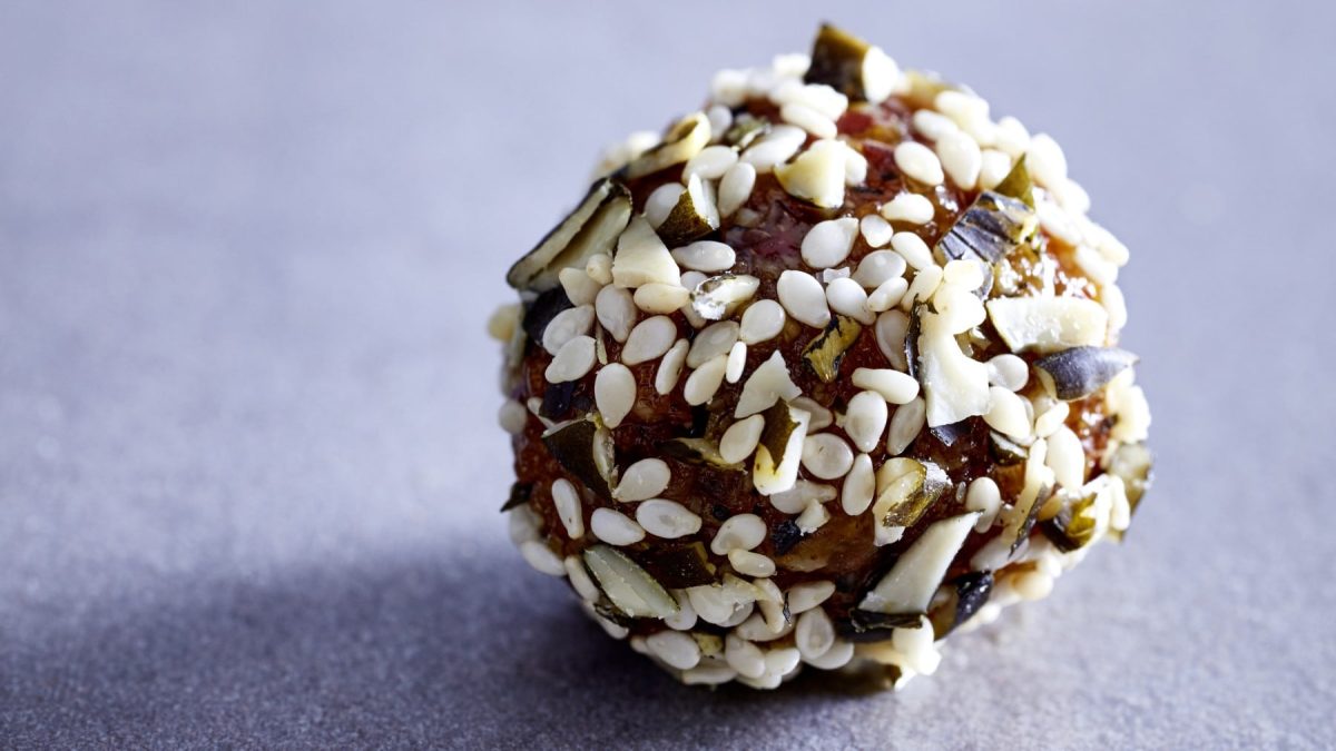Ein Aprikosen-Sesam-Ball auf einem grauen Hintergrund.