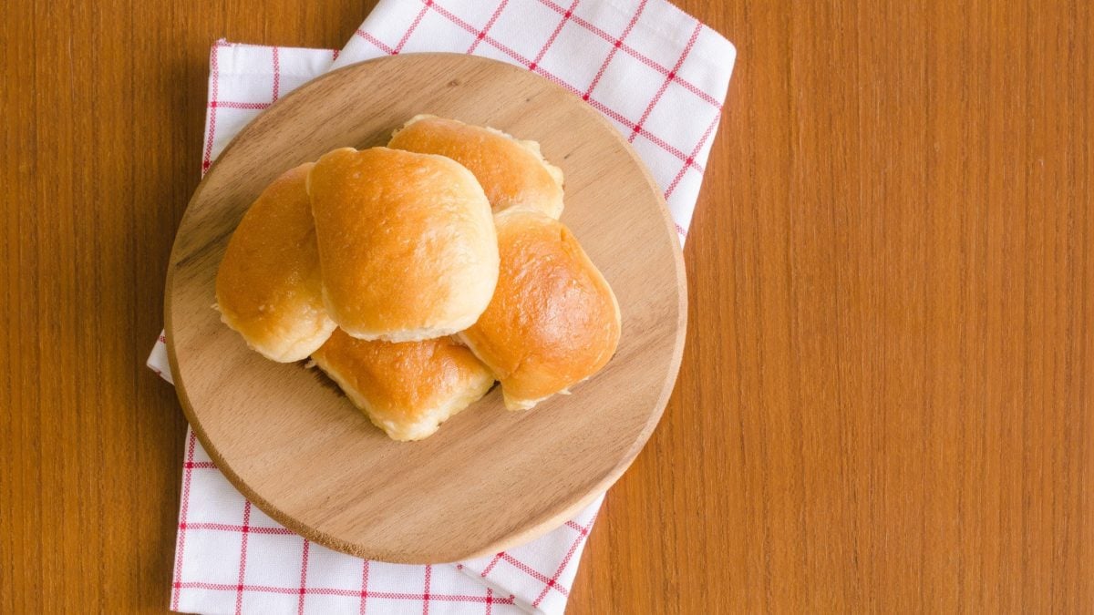 Das beste Brötchen zum Grillen vier Brötchen gestapelt auf einem Holzbrett, Tuch und hellem Untergrund. Draufsicht.