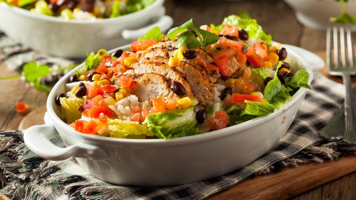 Eine weiße Auflaufform mit dem Burrito-Salat auf einem schwarz-weißen Tuch und Holztisch.