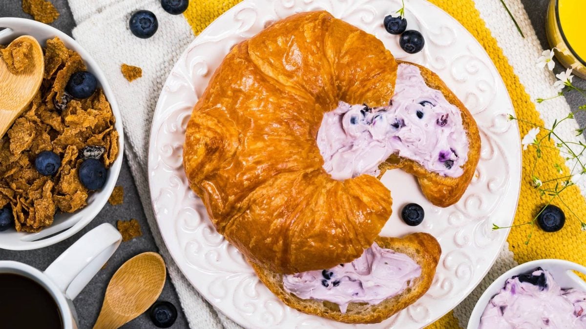 Draufsicht: Auf einem weißen Teller aus Porzellan liegt ein aufgeschnittenes Croissant mit Blaubeer-Thymian-Creme.