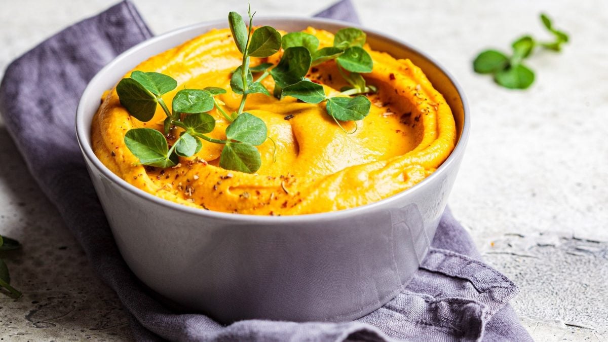 Eine graue Schale mit dem Mandel-Curry-Dip und Kresse auf einem grauen Tisch mit grau-blauem Küchentuch.