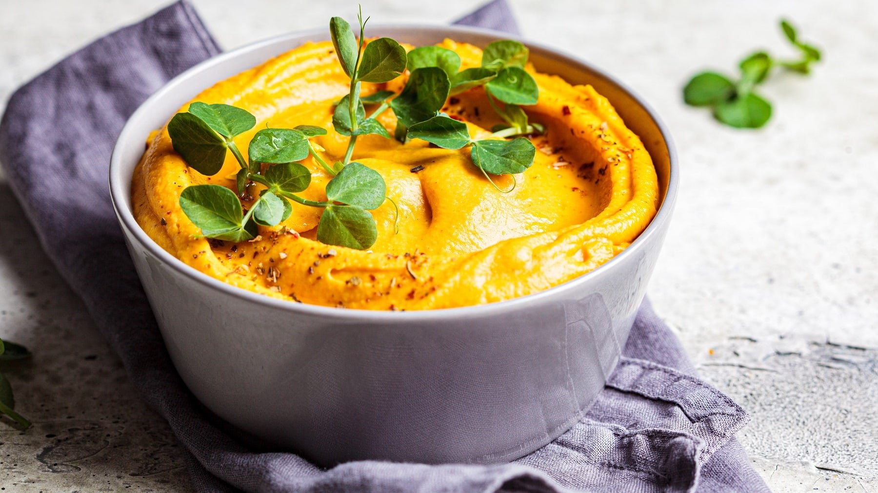 Eine graue Schale mit dem Mandel-Curry-Dip und Kresse auf einem grauen Tisch mit grau-blauem Küchentuch.