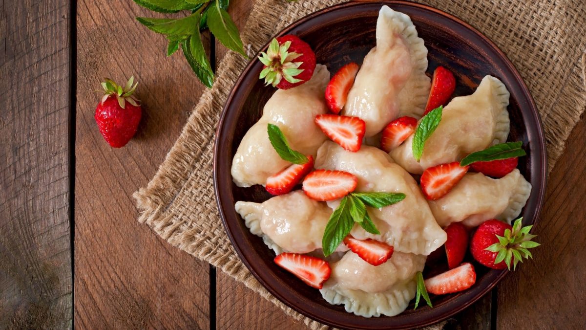 Erdbeer-Minze-Ravioli garniert mit Erdbeerscheiben und Minzblättern in einer dunklen Schüssel auf Stoff mit Holzuntergrund.