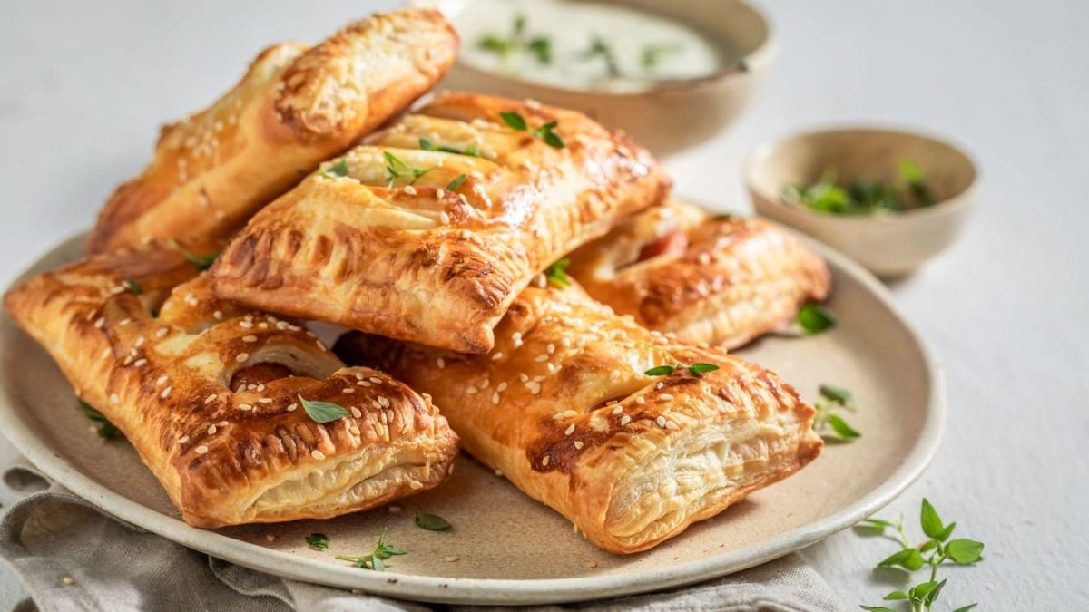 Vier Hotdog Strudel mit Sesam und Thymian auf Teller und hellem Untergrund. Draufsicht.