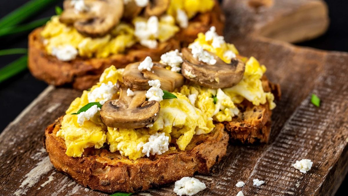 Zwei Scheiben mit dem Eiweißbrot und Hüttenkäse-Rührei auf einem dunklen Holzbrett.