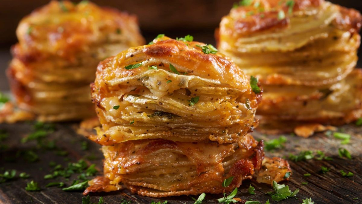 Kartoffelstapel mit Gruyère bestreut mit Petersilie auf Holzplatte.