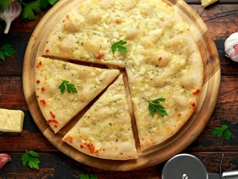Auf einem Holzteller ist eine Knoblauch-Käse-Pizza angerichtet. Sie ist mit Käse überzogen und goldbraun gebacken.