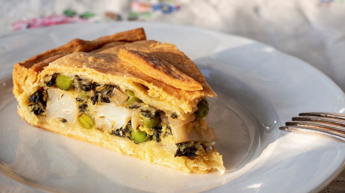 Ein Stück kroatische Mangold-Blumenkohl-Tarte auf einem Teller, daneben eine Gabel.