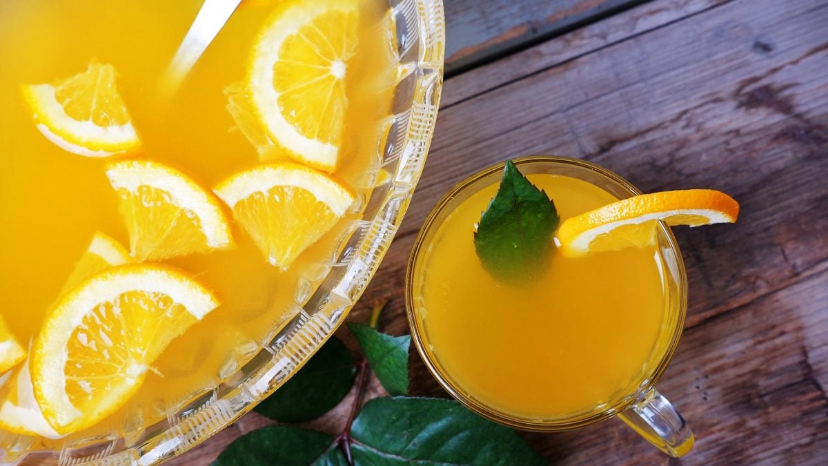 Eine große Glasschale mit dem gelben Punsch und daneben einem kleinen Glas mit dem Lillet Passion Punsch auf einem dunklen Holztisch.