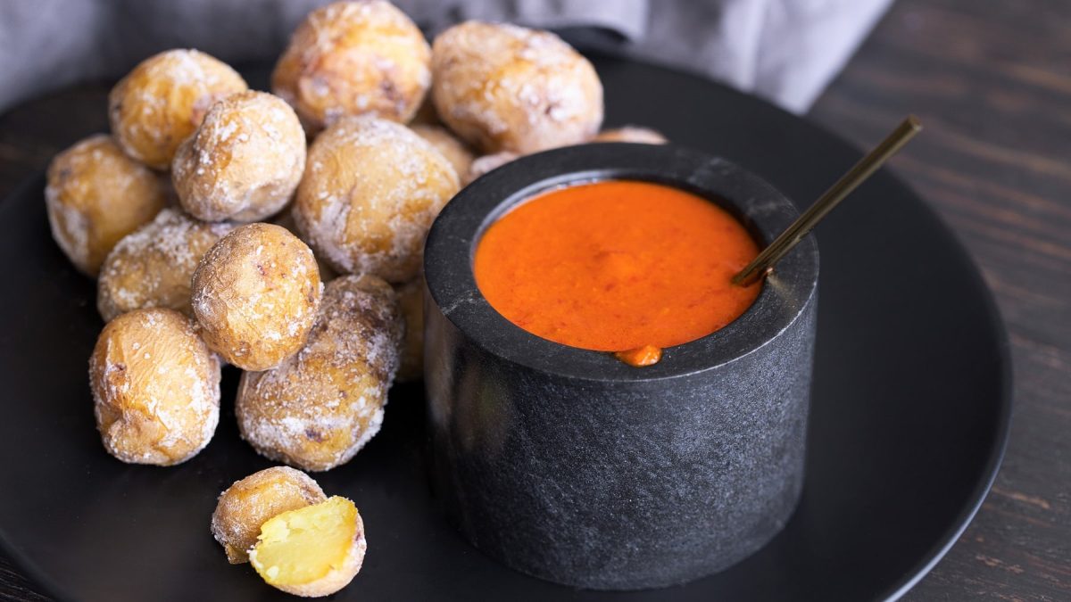 Ein schwarzer Teller mit Papas Arrugadas und dem rötlichen Dip Mojo rojo auf dunklem Holztisch.