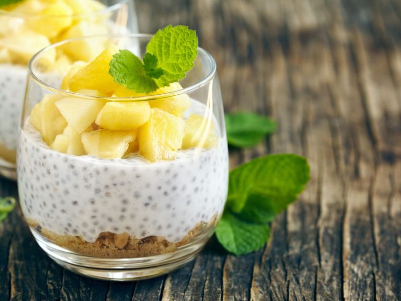 Ein Glas mit Piña Colada Overnight Oats auf einem Holztisch.
