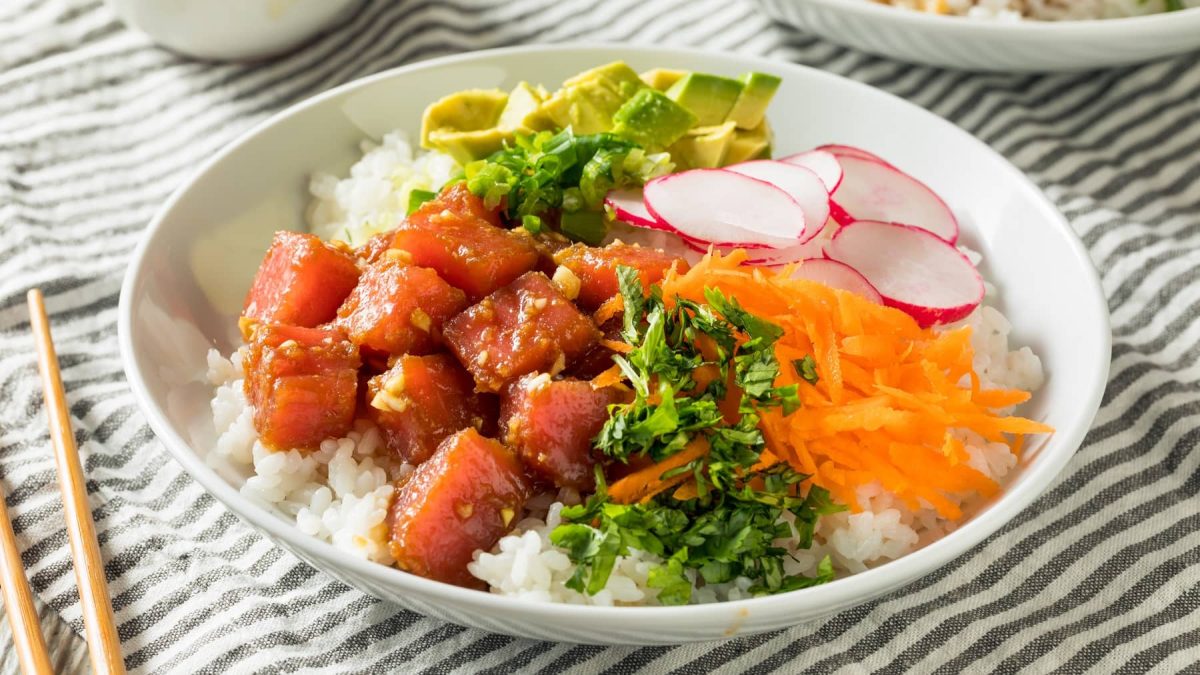 Eine weiße Schüssel mit der Poke Bowl auf einer weiß-grau gestreiften Tischdecke.