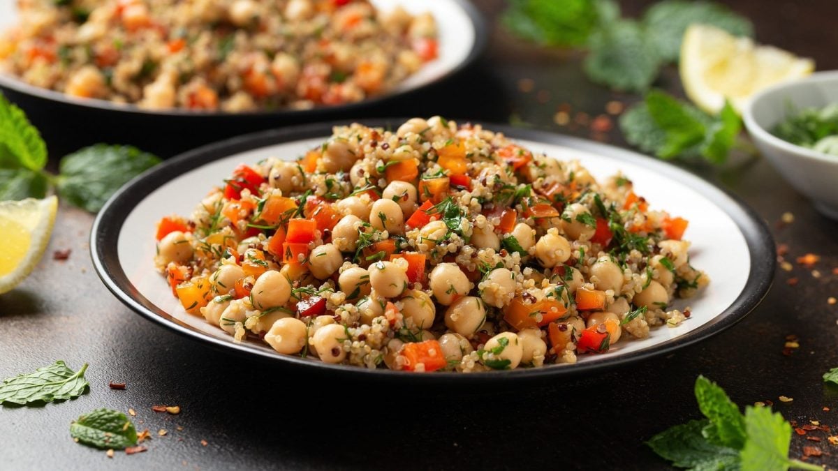Zwei Teller Thai-Quinoa-Salat mit Paprika und Kichererbsen und Kräutern, daneben liegen frische Minze und Zitronenspalten.