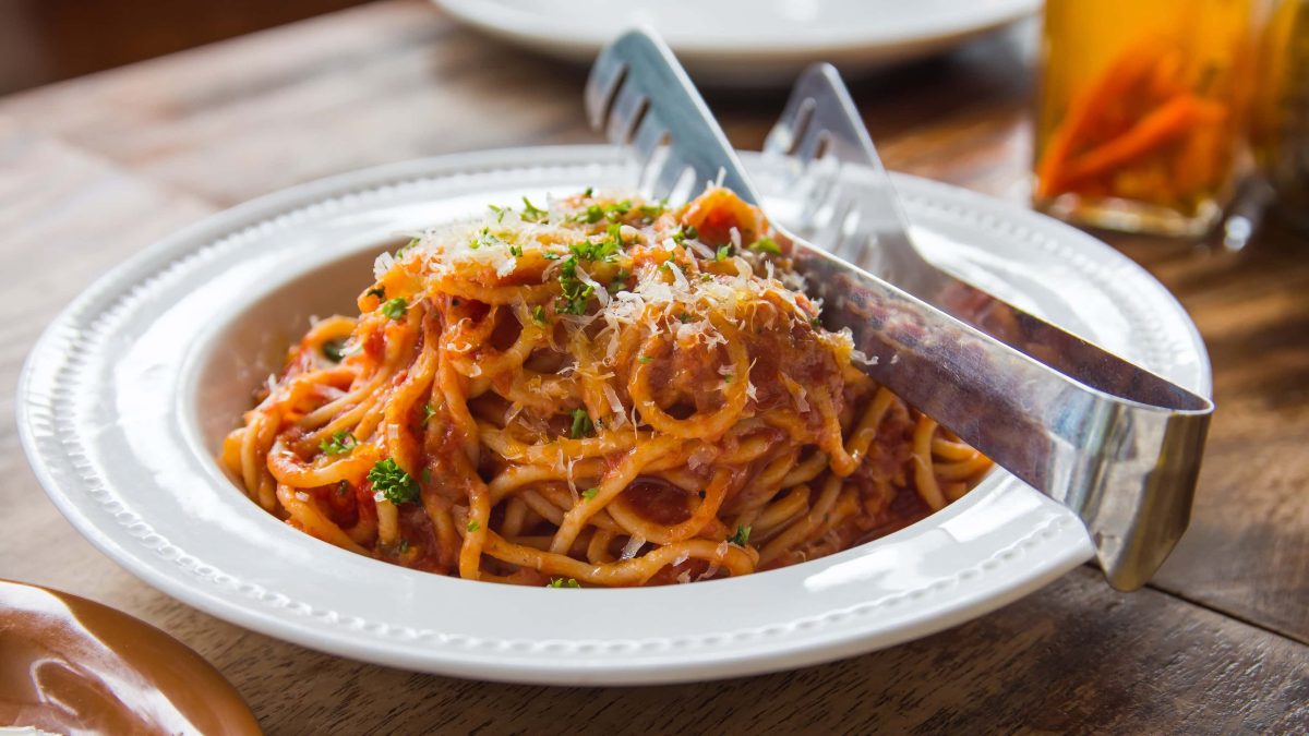 Thunfisch-Bolognese bestreut mit Parmesan und frischer Petersilie auf weißem Teller mit einer Nudelzange.