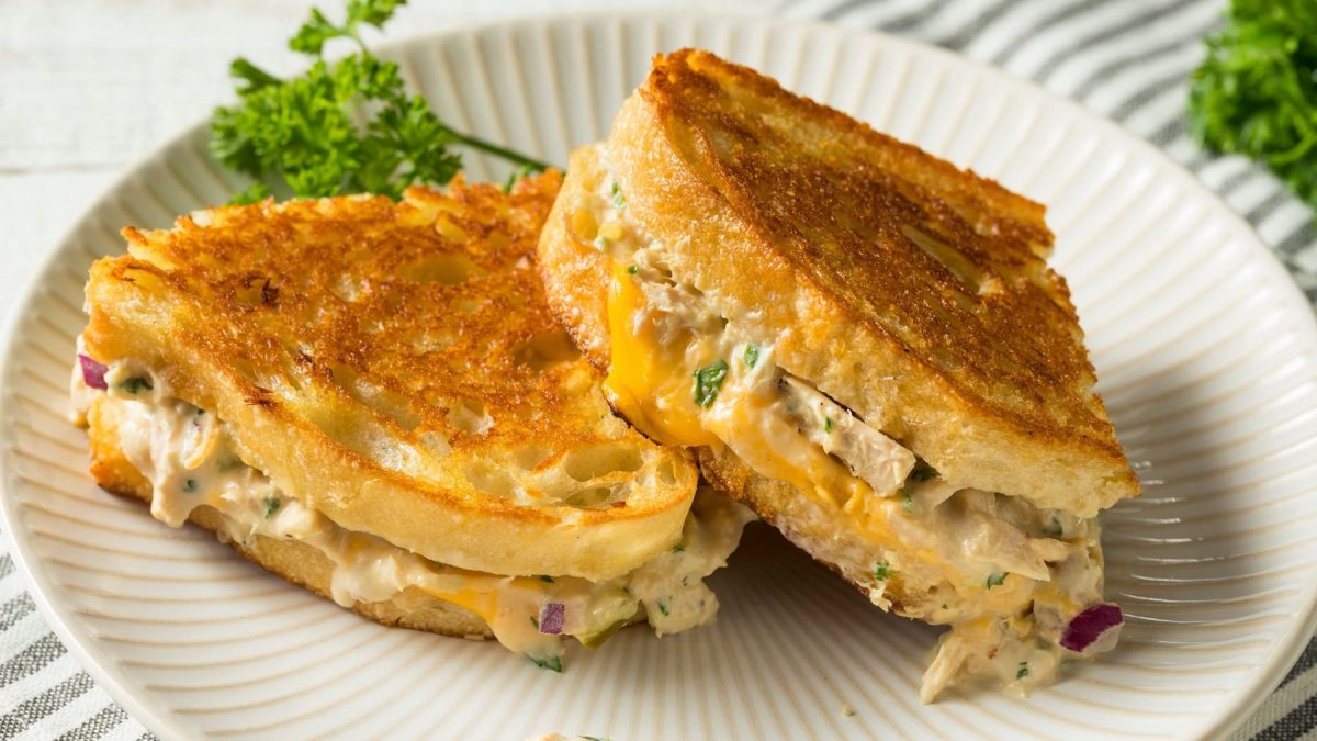 Das Tuna Melt Sandwich auf einem weißen Teller mit hellem Untergrund. Im Hintergrund etwas frische Petersilie.