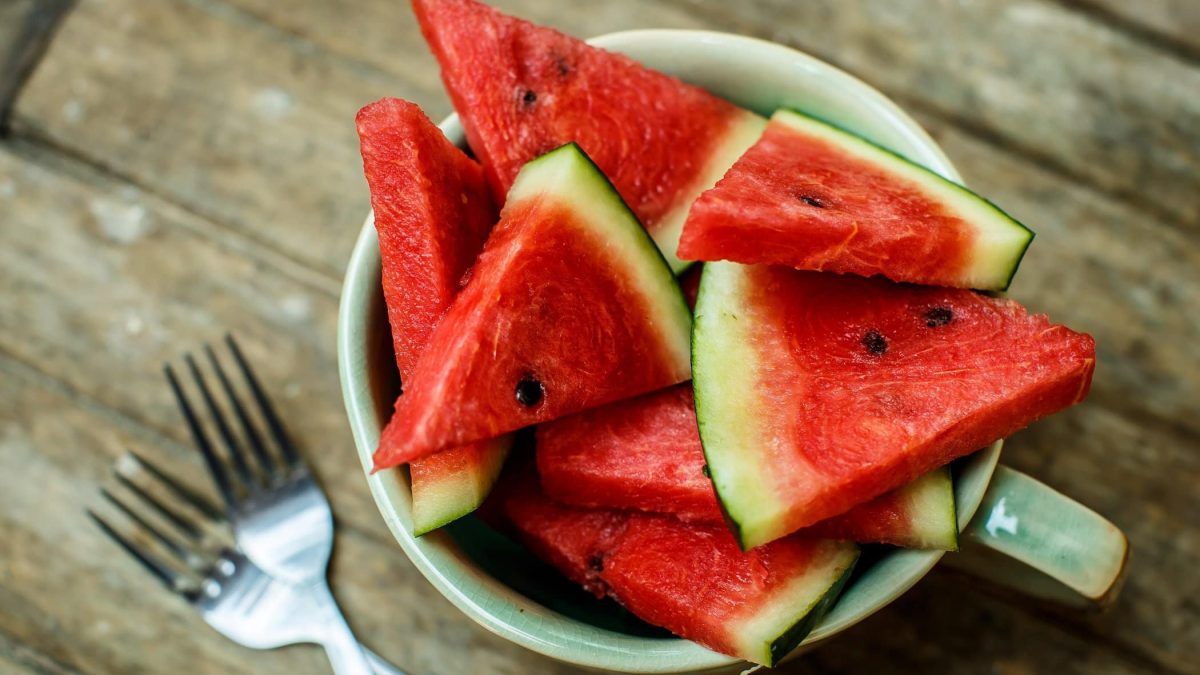 Frontalsicht: Auf einem Untergrund aus Holzplanken steht eine weiße Schüssel mit angeschnittener Wassermelone.