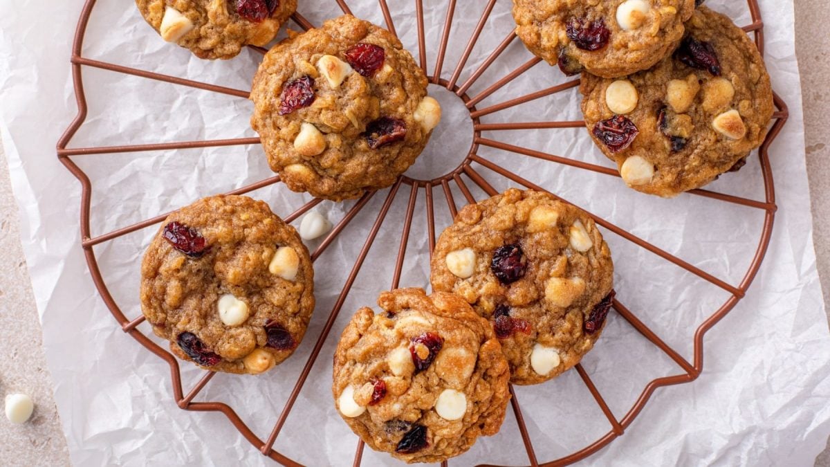 Draufsicht: Weiße-Schokolade-Cranberry-Cookies auf einem Gitter, darunter weißes Backpapier auf hellem Untergrund.
