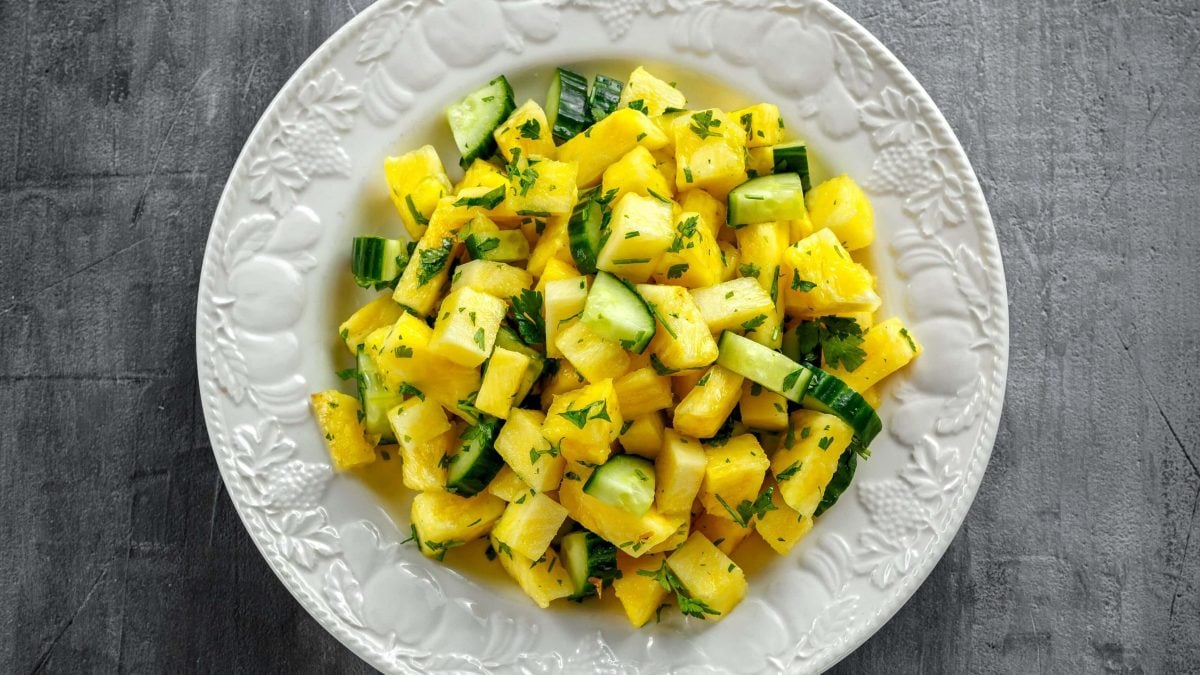 Ein weißer Teller mit dem Ananas-Gurken-Salat auf grauem Untergrund direkt von oben fotografiert.