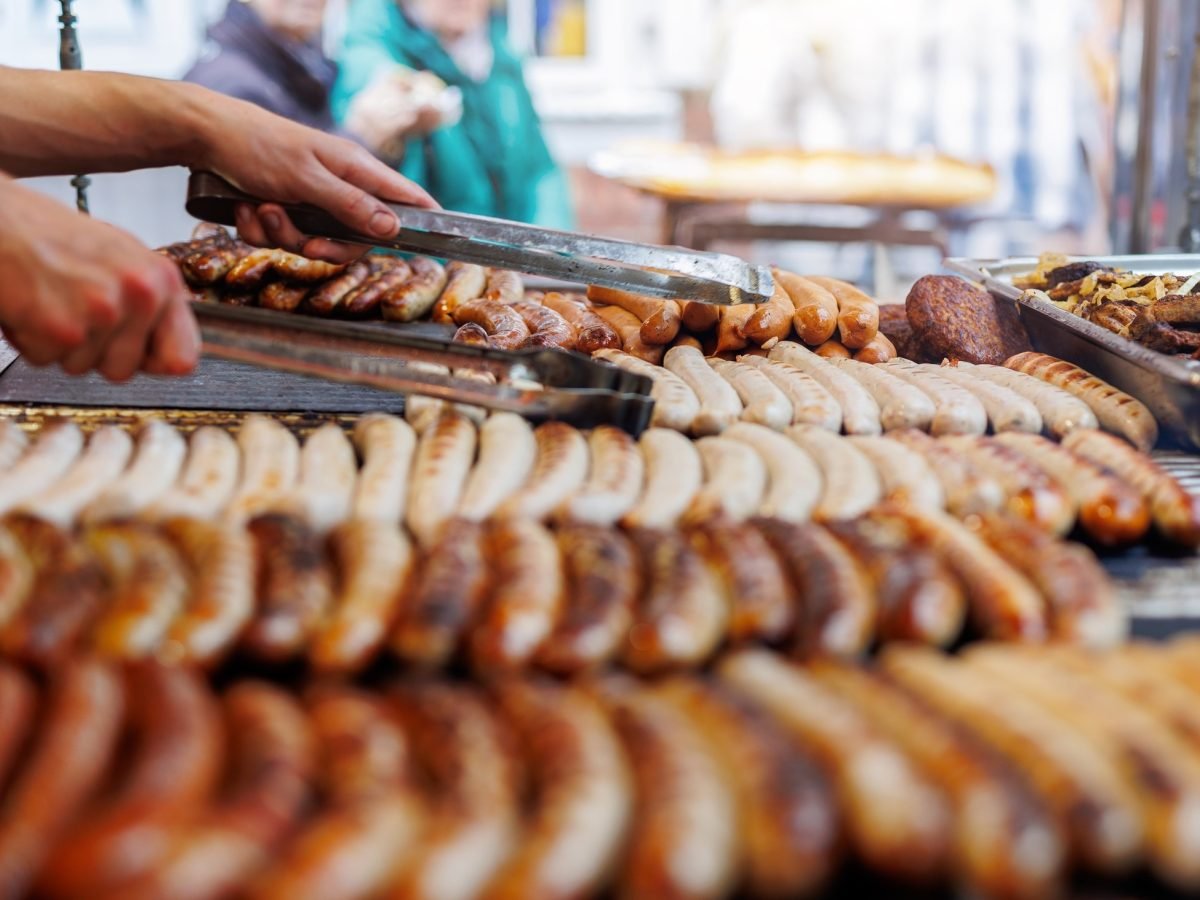 Frontal: sehr viele Bratwürste auf einem Grill / Streetfood-Anmutung /