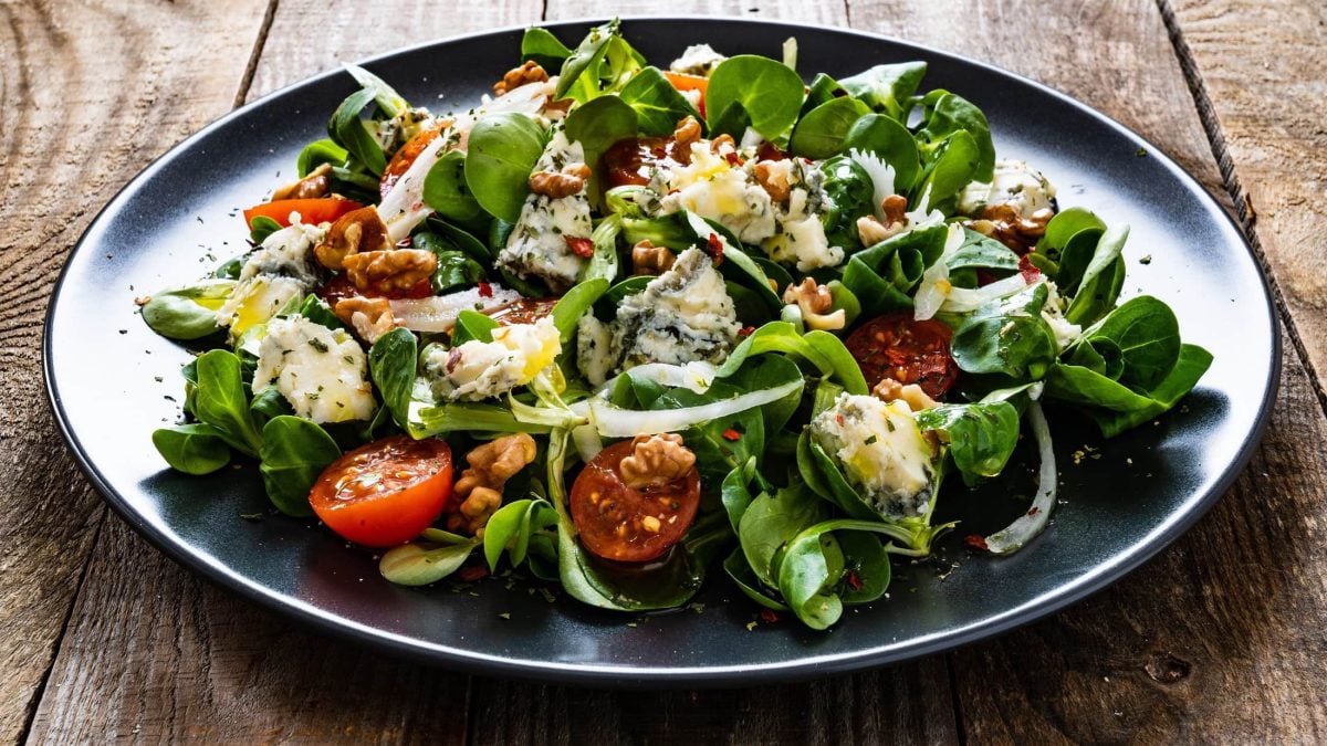 Schräge Draufsicht: ein dunkler Teller mit Feldsalat mit Roquefort, Tomaten, schwarzem Sesam und Walnüssen.