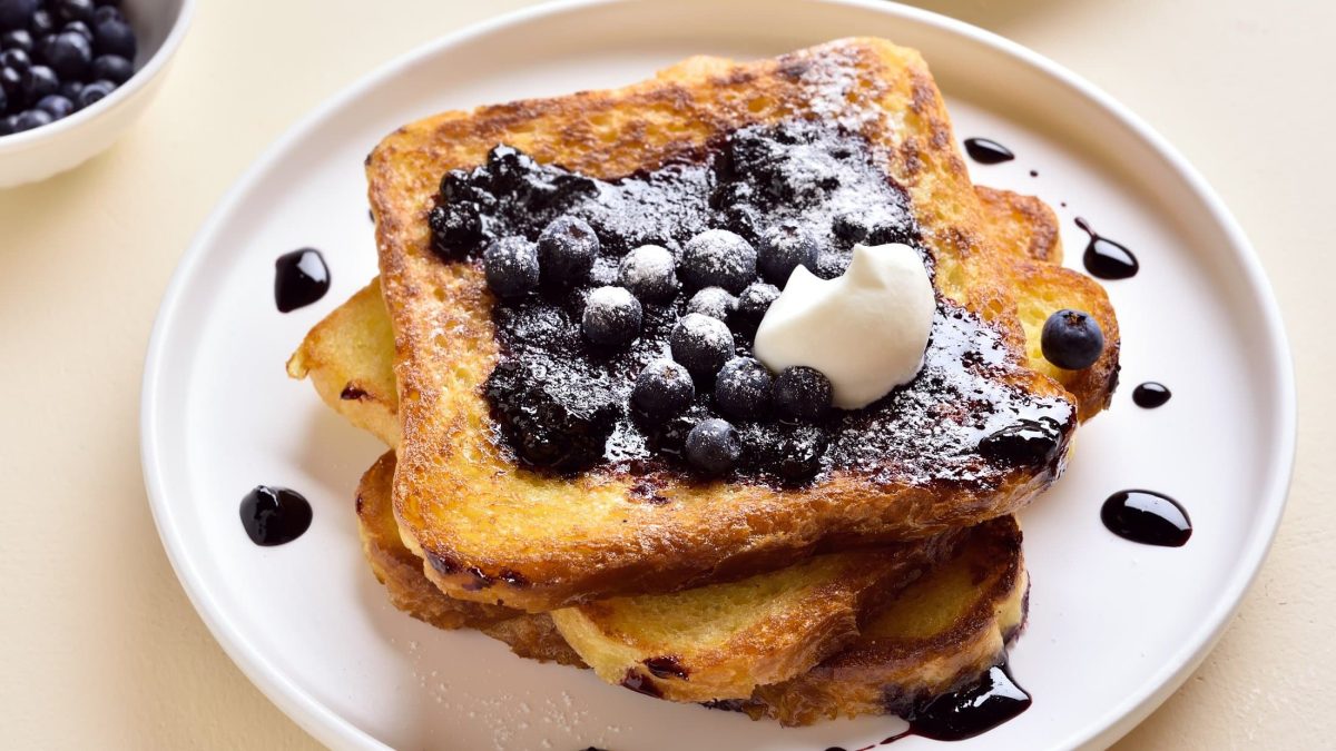 Draufsicht: ein weißer Teller mit einem French Toast mit Heidelbeeren und einem Klecks Sahne.