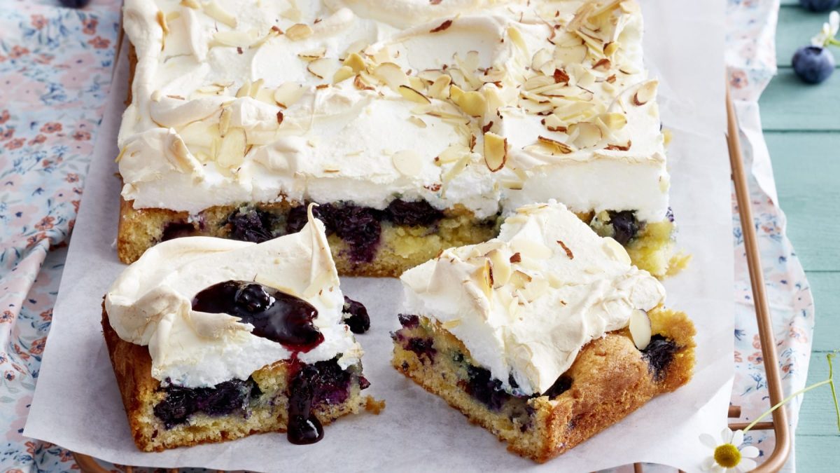 Angeschnittener Heidelbeer-Baiserkuchen auf hellem Untergrund.