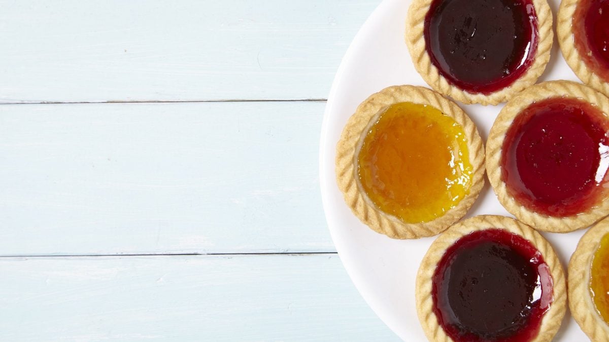 Draufsicht: Weißer Untergrund aus Holz, weißer runder Teller, auf dem runde Küchlein, die mit Marmelade gefüllt sind, liegen.