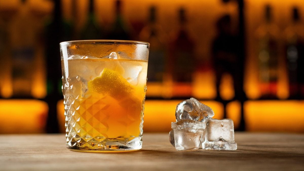 Ein Glas mit der Lynchburg Lemonade auf einem Holztresen. Im Hintergrund unscharf weitere Flaschen und Gläser im Regal zu erkennen.