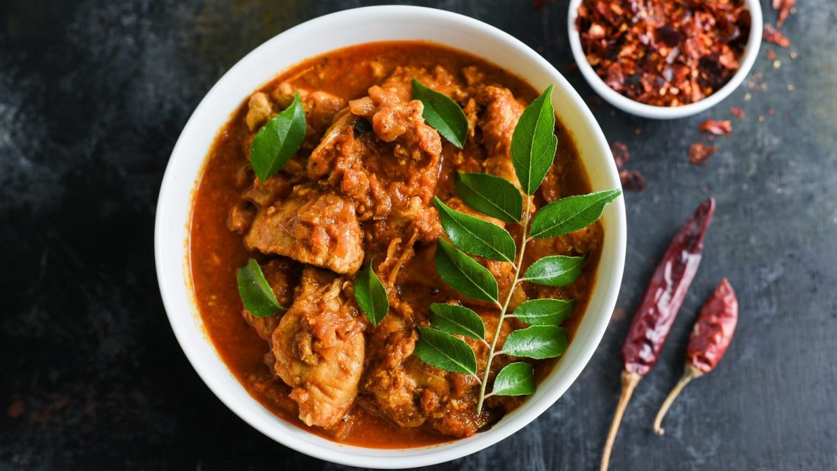Ein tiefer Teller mit Chicken Madras auf einem dunklen Tisch.