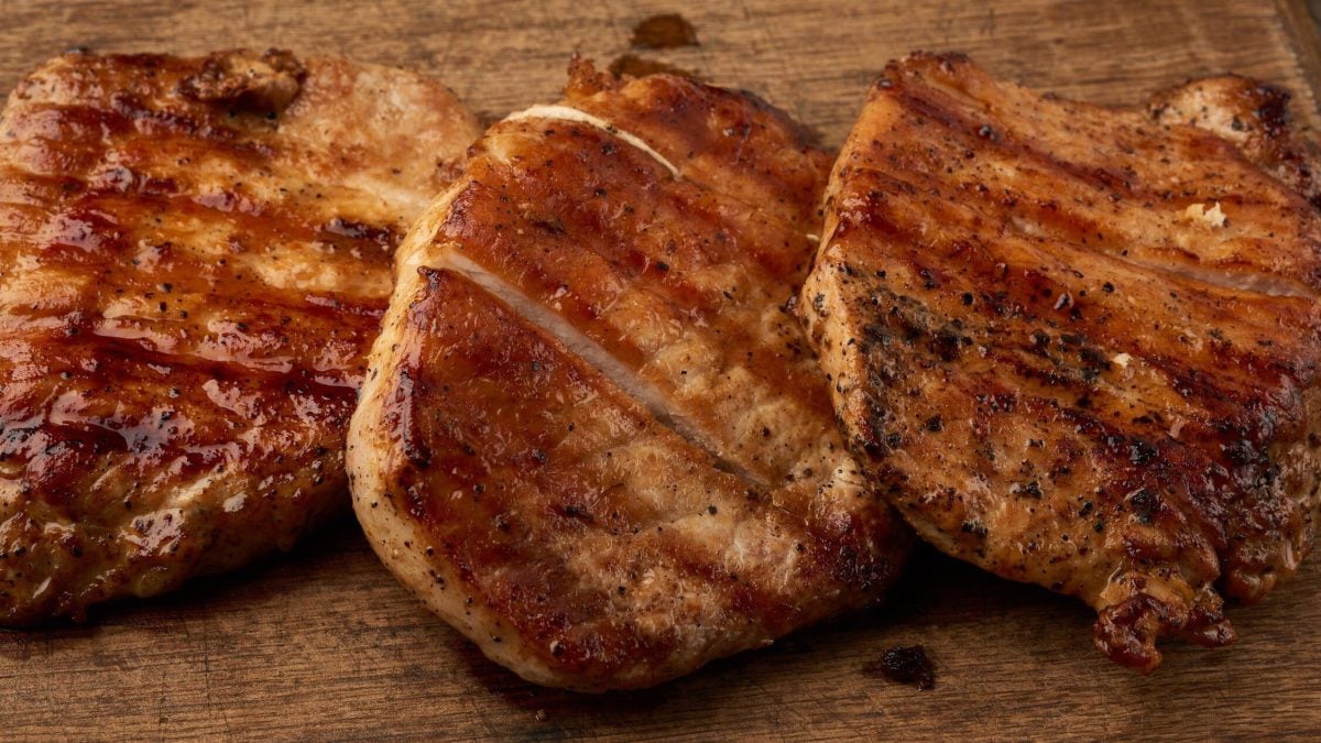 Magere, gegrillte Schweinesteaks in Paprika-Senf-Marinade aus dem Schweinelachs auf Holzbrett. Draufsicht.