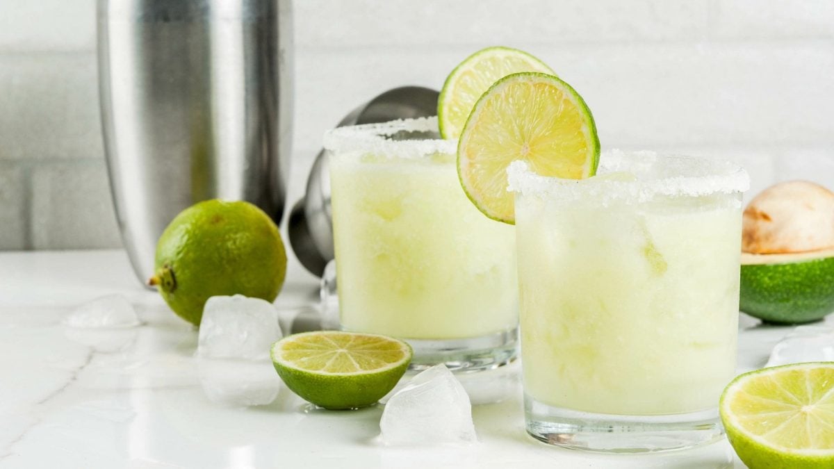 2 Gläser Margarita-Bowle mit Prosecco Eis und Limetten, mit Salzrand,daneben halbierte Limetten und ein Shaker.