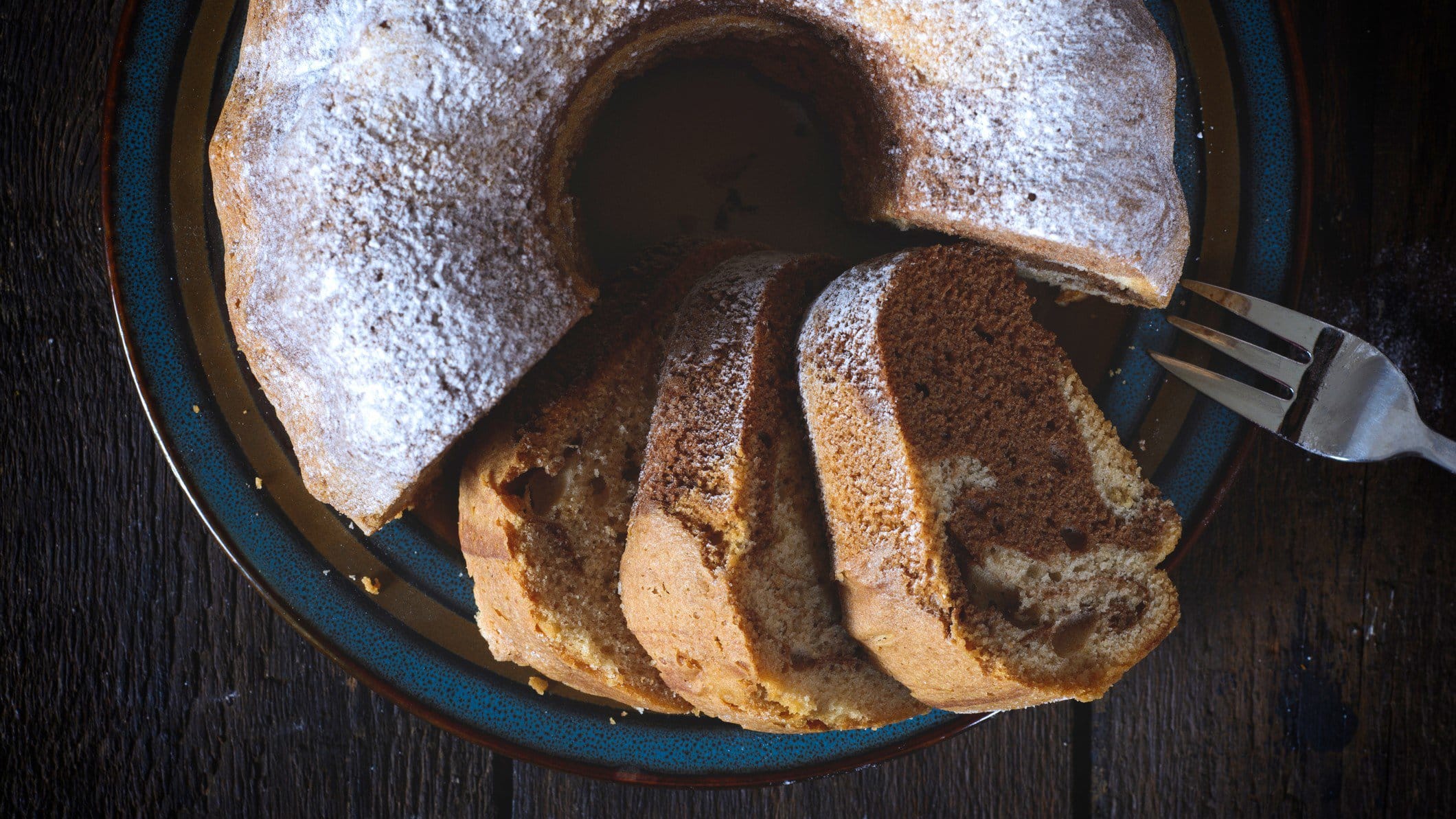 Marmor-Schüttelkuchen mit Puderzucker von oben auf dunklem Holz.