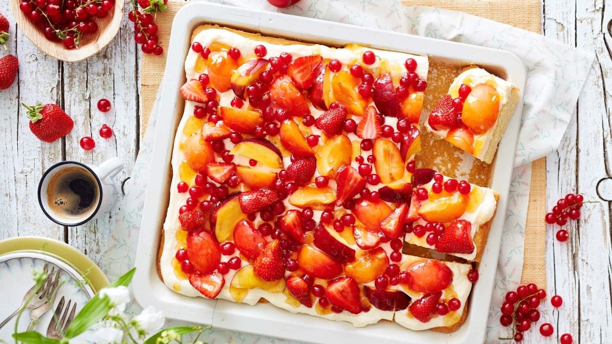 Draufsicht: Obst-Pudding-Schnitten in weißer Form auf hellem Holzuntergrund, drum herum Tasse Kaffee, Geschirr und Beeren.
