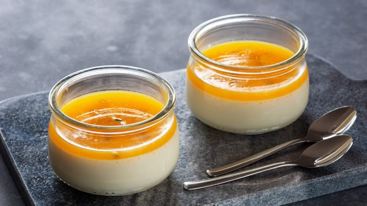 Zwei Dessertgläser mit Panna Cotta mit Passionsfrucht auf einem Steintablett.