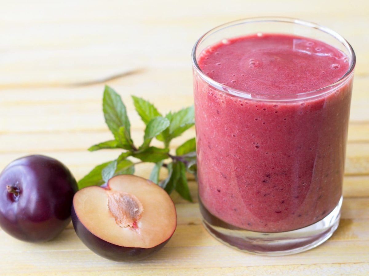 Pflaumen-Smoothie mit Heidelbeere, Minze und Basilikum in einem Glas auf Holztisch. Im Bild frische Minze und Pflaumen. Draufsicht.