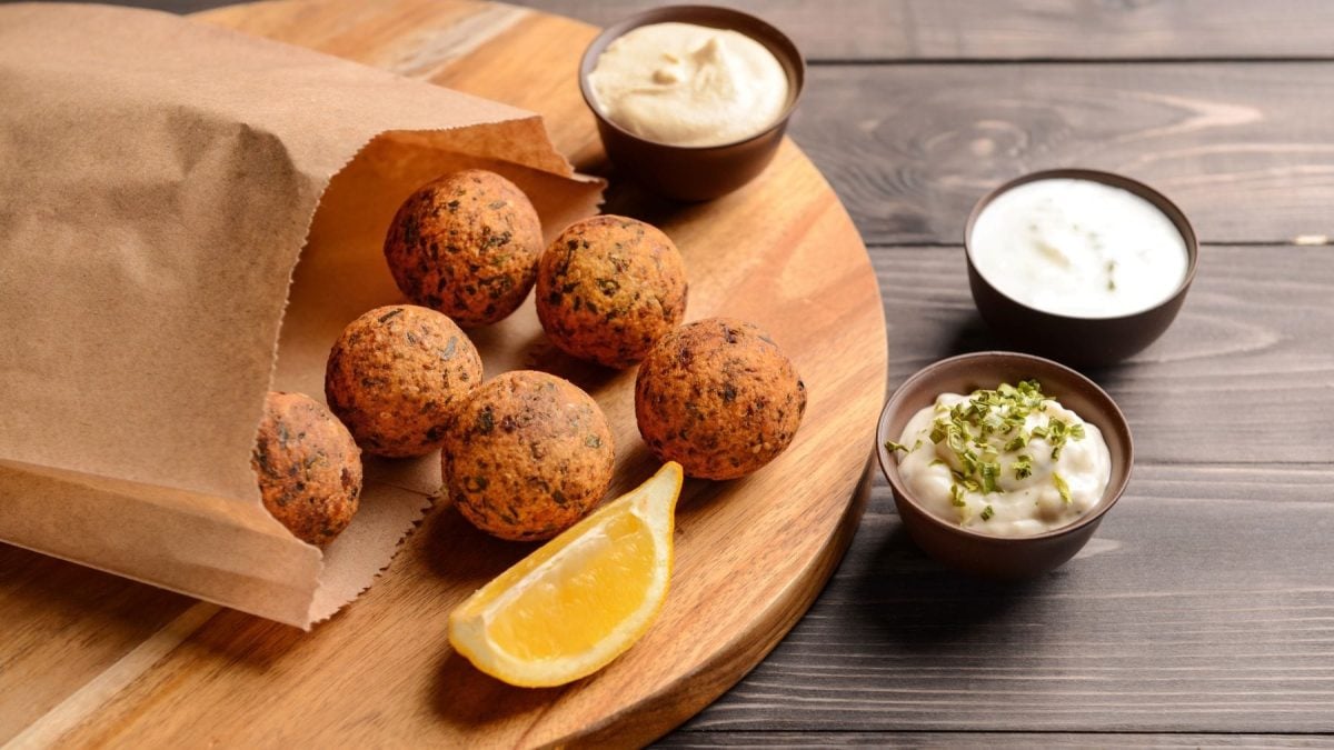 Popcorn Falafel aus Mais und Popcorn Kitchen Impossible in einer Papiertüre auf Holzbrett. Im Bild auf Holztisch dreierlei Dips und eine Zitronenspalte. Draufsicht.