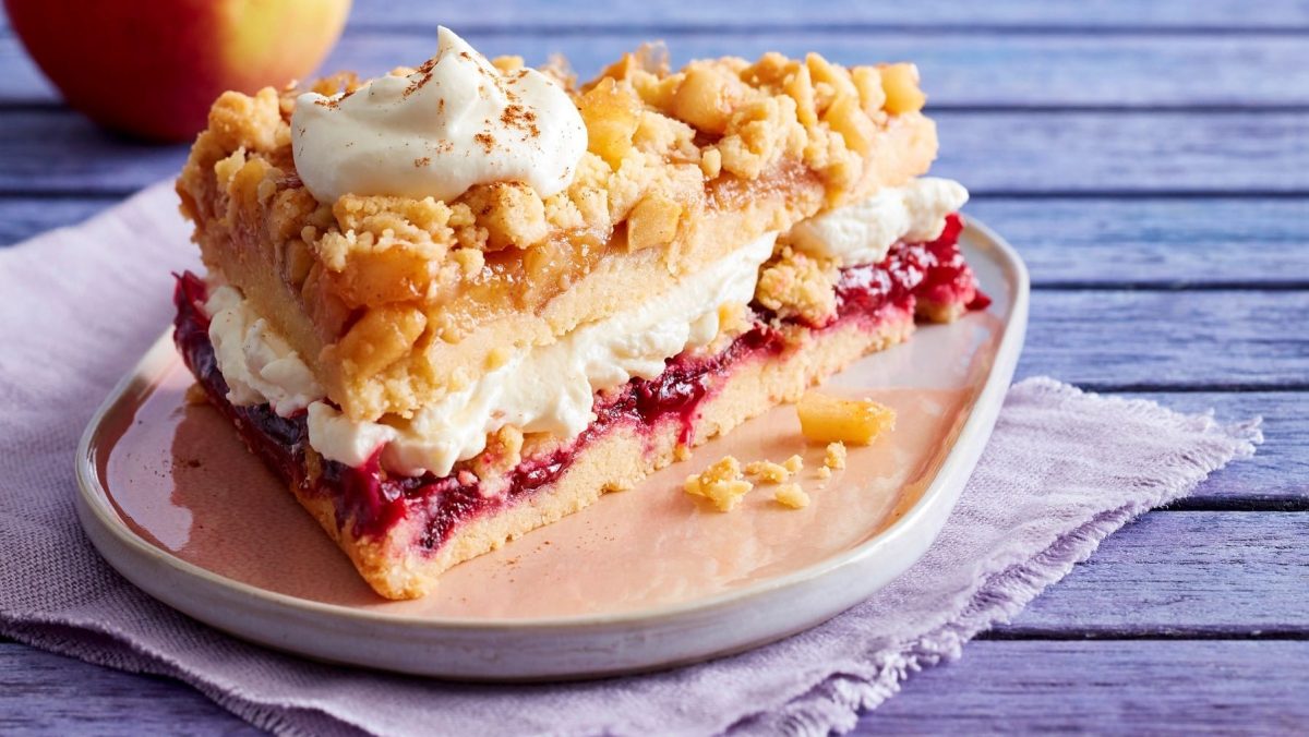 Ein Stück Prasselkuchen mit Vanille-Mascarpone-Creme auf einem Teller, darunter ein Tuch, blauer Holzuntergrund.