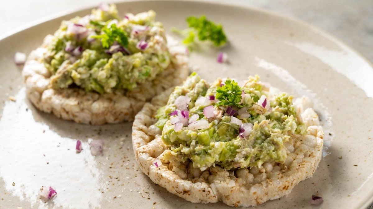 Zwei Reiswaffeln mit dem Avocado-Thunfischsalat auf einem weißen Teller und hellem Untergrund.