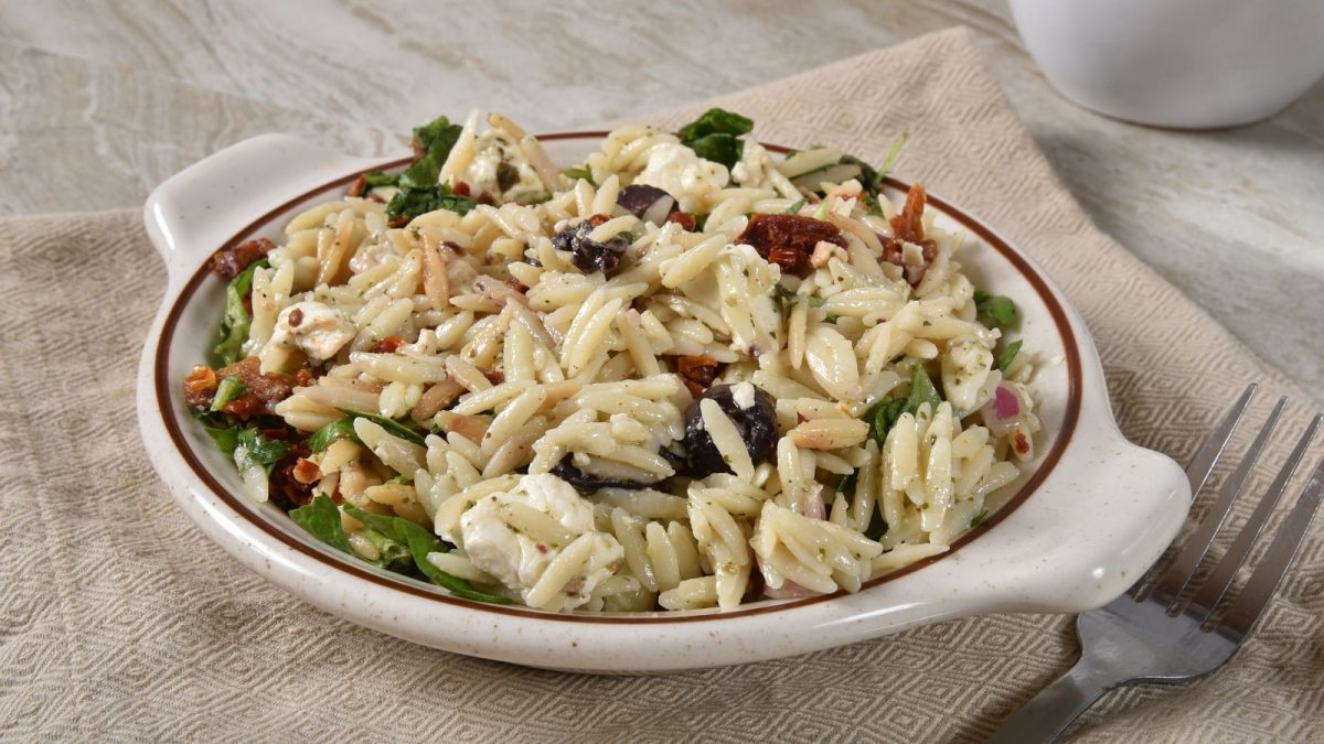 Ein tiefer Teller mit Orzo-Pasta mit getrockneten Tomaten und Mozzarella.