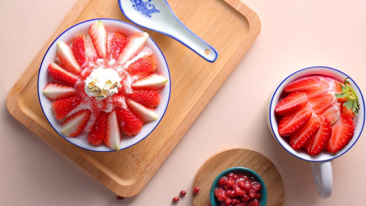 Ein Holztablett mit Strawberry Bingsu auf einem rosafarbenen Untergrund.