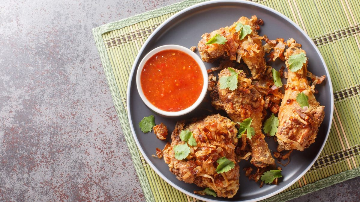Thai Thai Fried Chicken Hat Yai Style mit Röstzwiebeln und Sauce auf grauem Teller, Matte und grauem Tisch. Draufsicht.