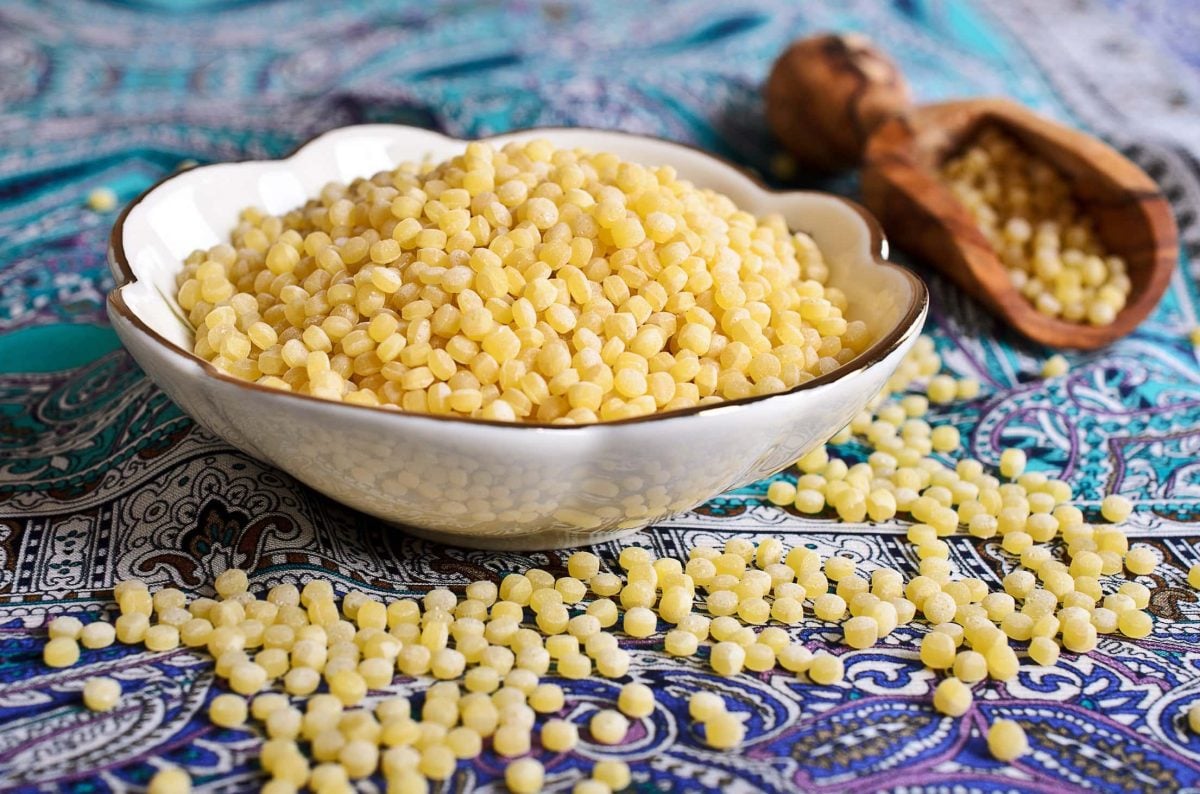 Auf einem orientalisch angehauchtem Untergrund steht eine Schüssel Ptitim. Der israelische Couscous ist zudem drum herum verstreut.