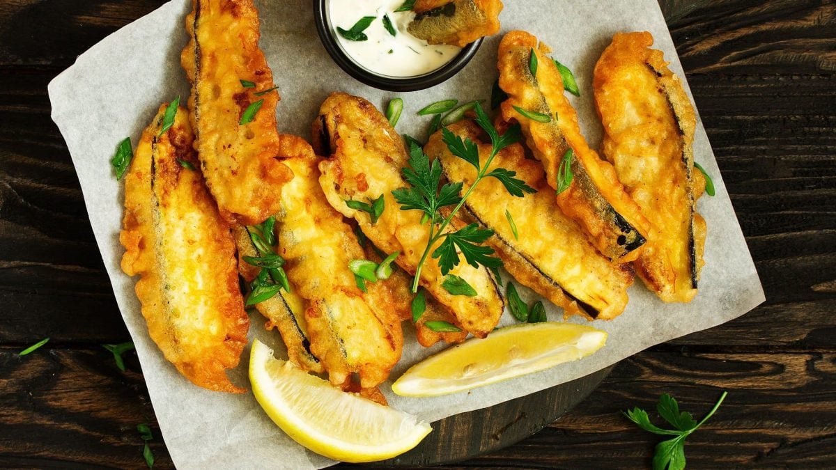 Draufsicht: In der Pfanne gebratene Zucchinistifte, die in Asien Zucchini-Karaage heißen. Drum herum liegen Zitronenschnitze und Petersilie.