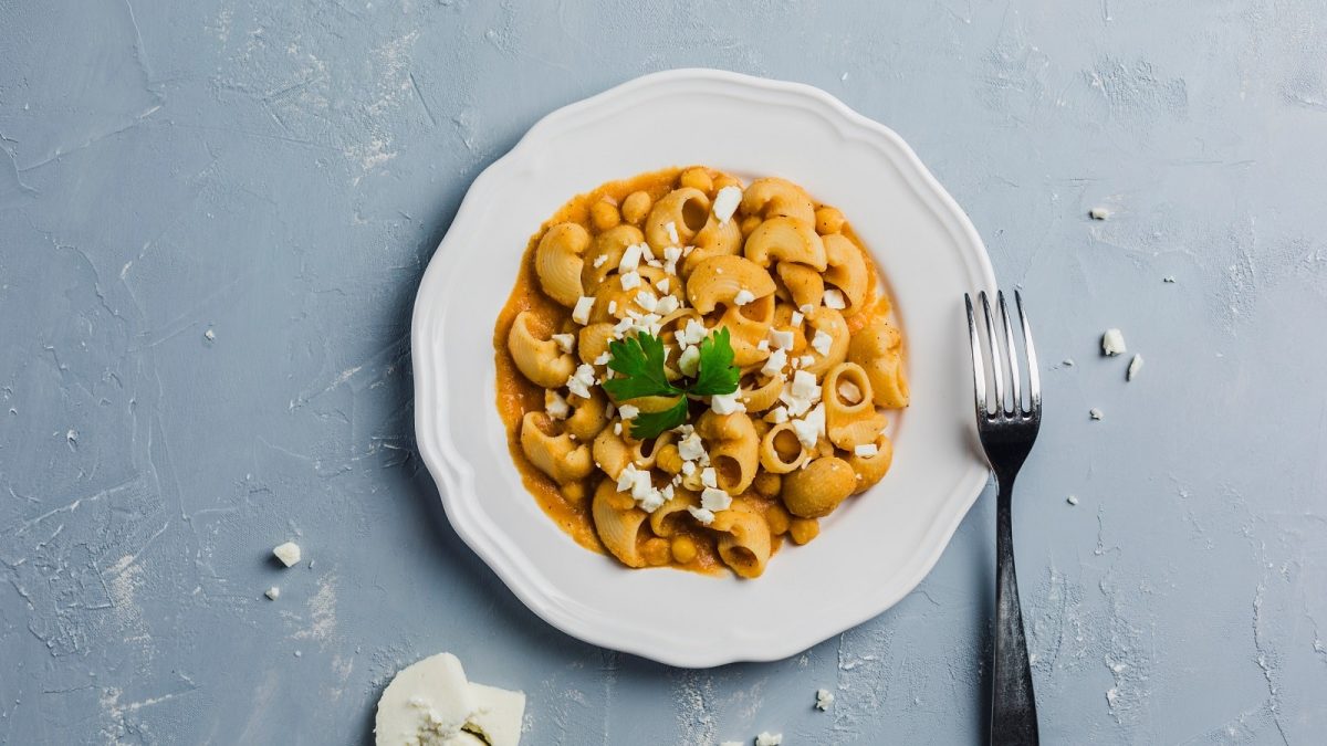 Ein weißer Teller mit Pasta mit Kichererbsensauce auf einem grauen Tisch.