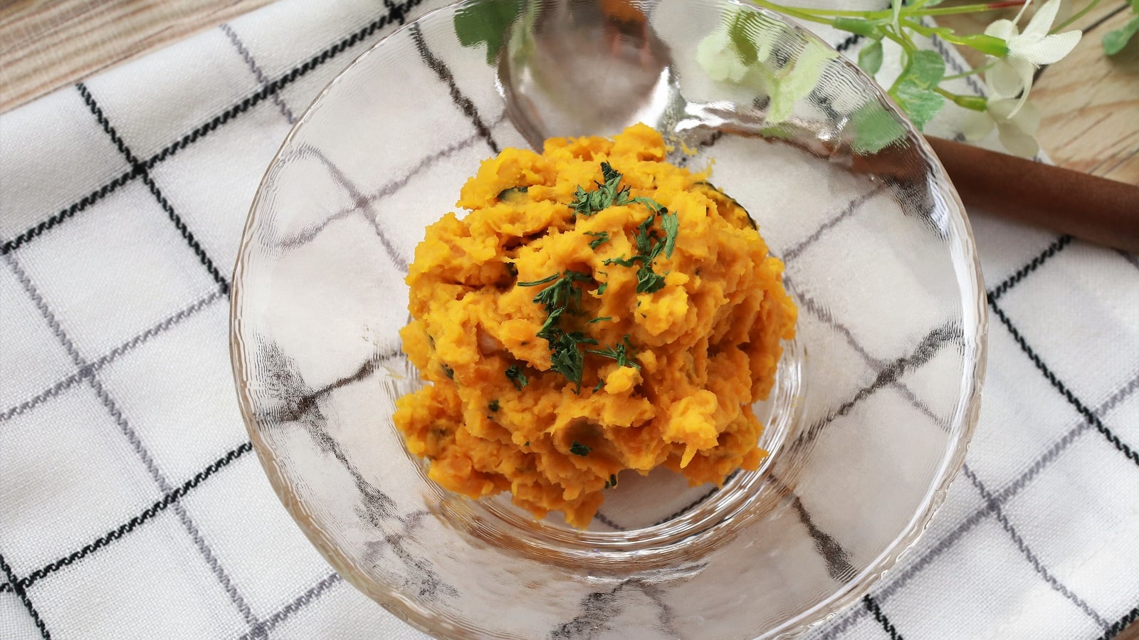 Eine Glasschüssel mit Kabocha-Salat auf einem karierten Geschirrtuch.