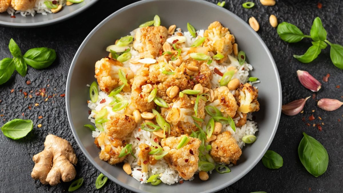 Ein tiefer grauer Teller mit einer Portion Kung Pao Blumenkohl auf einem dunklen Tisch.