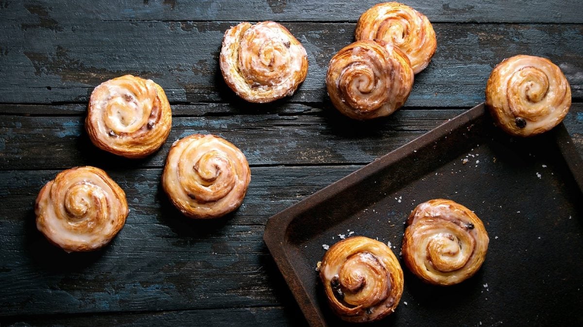 Blätterteig-Schnecken mit Erdnussmus und Marmelade auf einem hölzernen, dunklen Hintergrund. Rechts ein schwarzes Backblech.